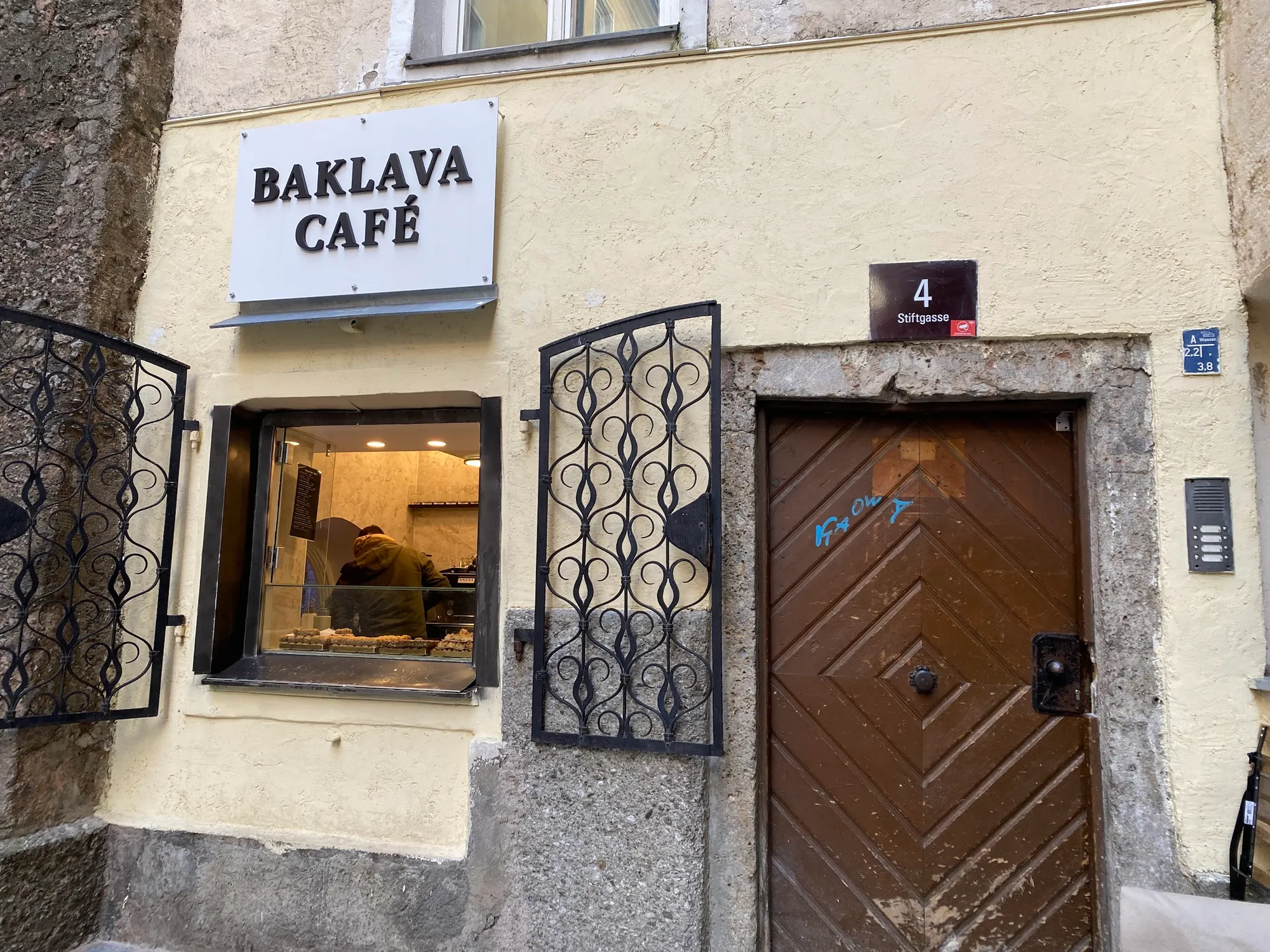 Das Baklava Café von außen: weißes Schild „Baklava Café“, ein kleines Fenster mit schmiedeeisernen Läden und die Hausnummer Stiftgasse 4