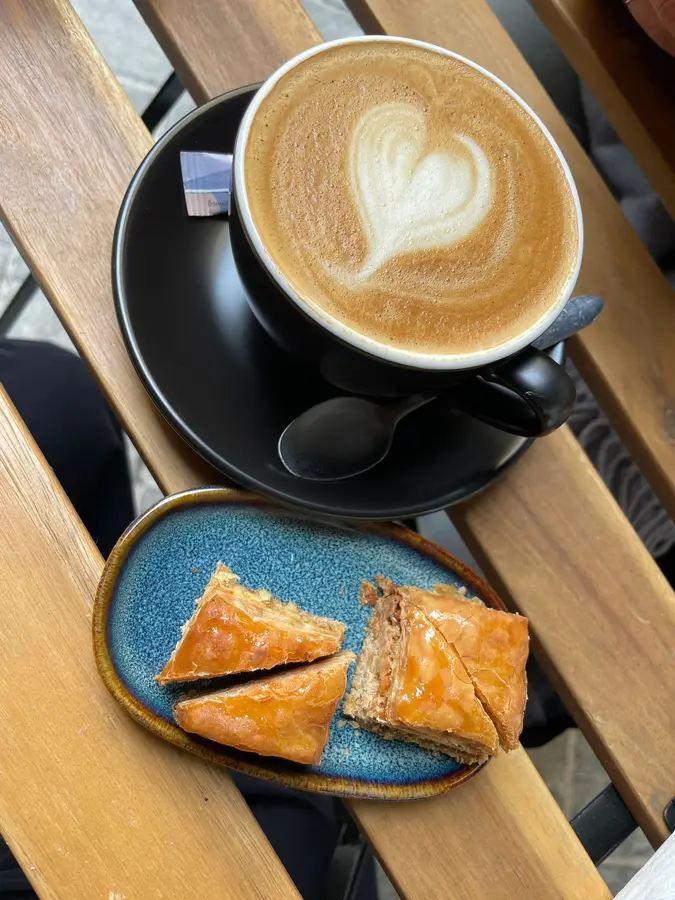 Cappuccino mit Herz-Latte-Art und Baklava auf einem blauen Teller